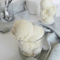 three scoops of ice cream sit in a glass on a table next to two spoons