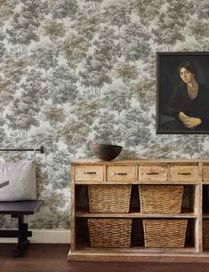 a painting on the wall next to a dresser with baskets in front of it and a chair