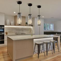 a large kitchen with an island and bar stools in the center, surrounded by wooden flooring