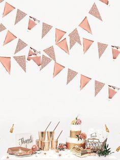 a table topped with cake next to a white wall and pink buntings hanging from the ceiling