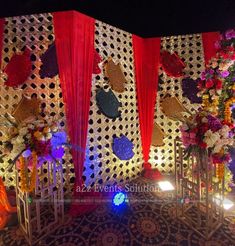 a decorated stage with red drapes and colorful flowers on it's sides, along with other decorations