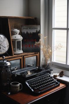 an old fashioned typewriter sitting on top of a wooden desk next to a window