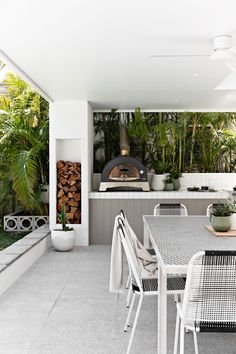 an outdoor kitchen and dining area with wood burning oven in the back ground, surrounded by greenery