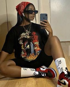 a woman sitting on the floor with her cell phone in her hand and wearing sneakers