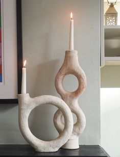 two white candles sitting on top of a table next to a vase and candle holder