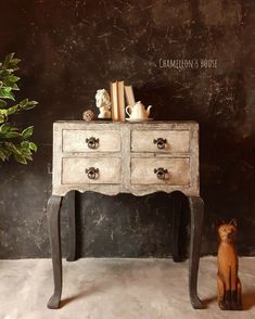 a small dog sitting in front of a table with two drawers and books on it