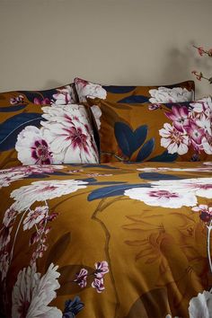 a bed with floral comforter and pillows on top of it next to a plant