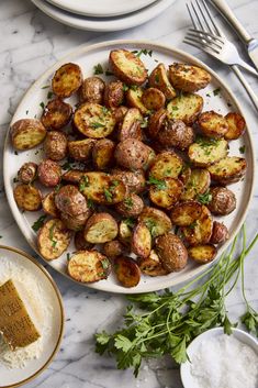 a white plate topped with potatoes and parsley next to two plates filled with bread