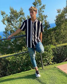 a young man standing on top of a lush green field next to a metal rail