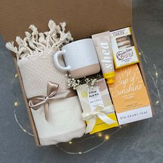 an open box with coffee, tea and other items in it on a table next to some string lights