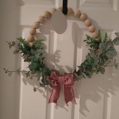 a wooden beaded wreath hanging on the front door with pink ribbon and greenery