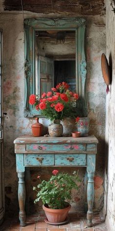 an old table with potted flowers on it in front of a mirror and window