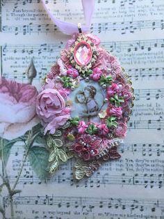 an ornament with pink flowers on top of sheet music paper and a ribbon