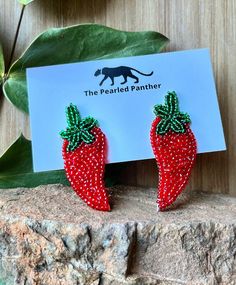 the beaded panther strawberry earrings are on display next to a card and some leaves