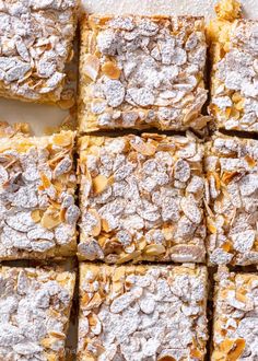 several square pieces of dessert with powdered sugar on top and almonds in the middle