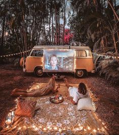 two people sitting on a blanket in front of a vw van with a screen