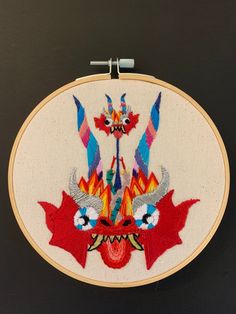 a colorful embroidered art piece hanging on a black wall next to a pair of scissors