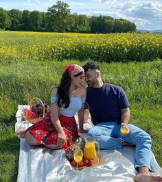 a man and woman are sitting on a blanket in the grass with fruit, drinks and juice