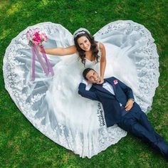 a man and woman laying on top of a white heart shaped blanket in the grass