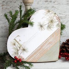 a heart shaped wooden decoration with pine cones and berries on the table next to it