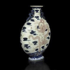 a white and blue vase sitting on top of a black table next to a wall