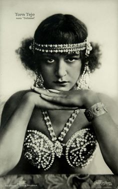 an old black and white photo of a woman with beads on her head, wearing a bra