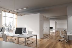 an empty office with desks and computer screens on the wall, in front of large windows