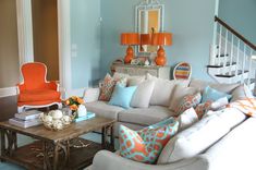 a living room filled with furniture next to a stair case and orange chairs in front of a white couch