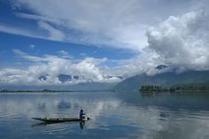 a man in a canoe on the water with mountains in the background and clouds in the sky