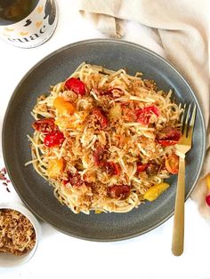 a plate full of pasta with tomatoes and other toppings next to a cup of tea