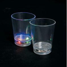 two shot glasses sitting next to each other on a black surface with lights in the background