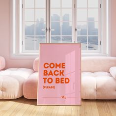 a pink poster with the words come back to bed placed in front of a white couch