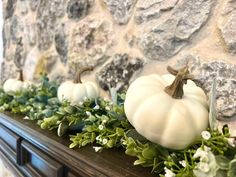 some white pumpkins and greenery are on a mantle in front of a stone wall