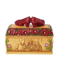 two red shoes sitting on top of a wooden box with flowers and leaves painted on it