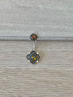 a silver belly ring with an orange and yellow flower on it's end, sitting on a wooden surface