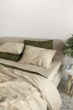 a bed with white sheets and pillows next to a potted plant