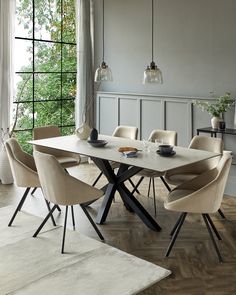 a dining room table with chairs and a vase on the side, in front of a large window