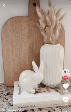 a white rabbit statue sitting on top of a counter next to a book and cutting board