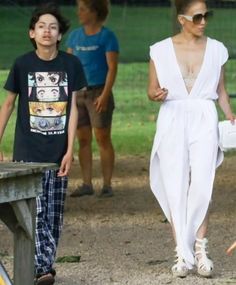 a woman in a white jumpsuit walking next to a boy with a baseball bat