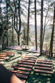 rows of wooden benches sitting on top of a grass covered field next to tall trees