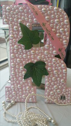 a pink letter decorated with pearls and leaves