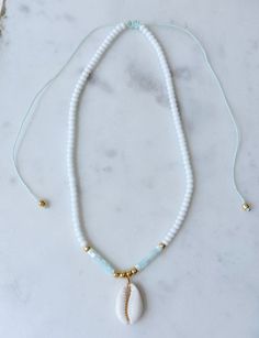 a white beaded necklace with a shell pendant on it's end, sitting on a marble surface