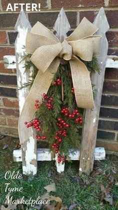 a wooden sign with a bow and berries hanging from it's side, in front of a brick wall