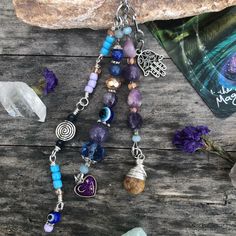 a necklace with various beads and charms on it sitting next to a book, rock and flowers