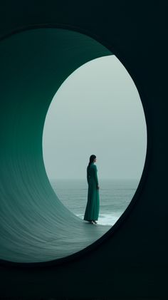 a woman in a long green dress is looking out at the ocean through a tunnel