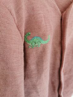 a pink sweater with a green dinosaur embroidered on it