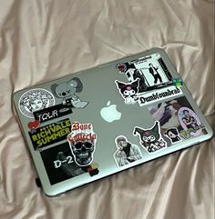 an apple laptop covered in stickers on a bed