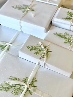 several wrapped presents with white bows and green leaves on them, all tied up together