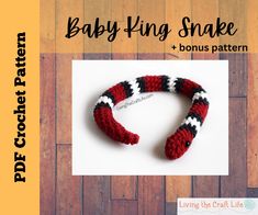 a red, black and white knitted snake on a wooden floor with the words baby king snake written across it