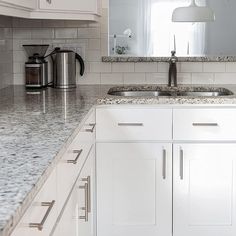 a white kitchen with granite counter tops and stainless steel appliances on the wall behind it